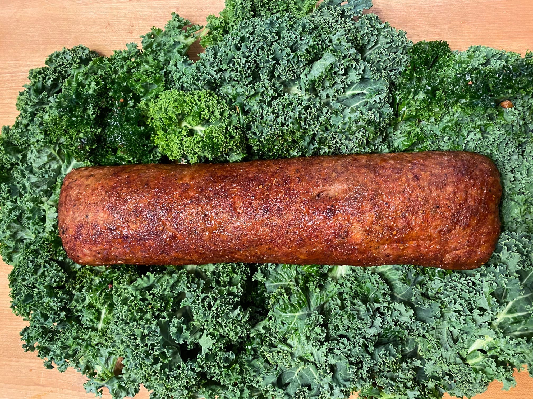 A sausage on top of some broccoli.